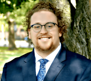 A man in a suit and tie standing next to a tree.