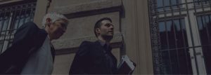 A man in black jacket holding papers near building.