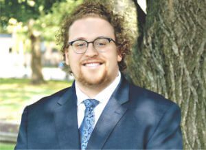 A man in a suit and tie standing next to a tree.