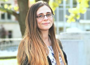A woman with glasses standing outside in front of trees.