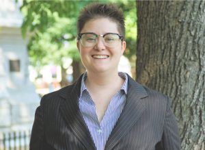 A woman in glasses and a suit standing next to a tree.