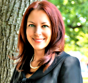 A woman with red hair standing next to a tree.