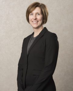 A woman in black jacket standing next to wall.