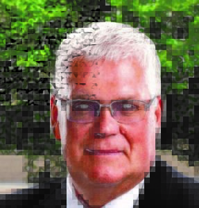 A man with white hair and glasses in front of trees.