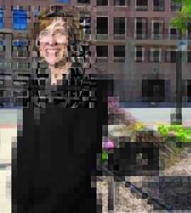 A woman in black jacket standing on sidewalk next to building.
