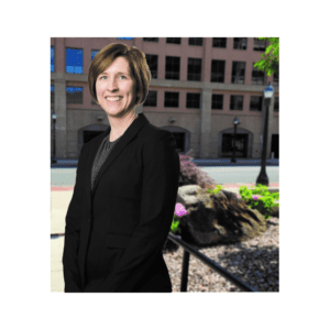 A woman in black jacket standing on sidewalk next to building.