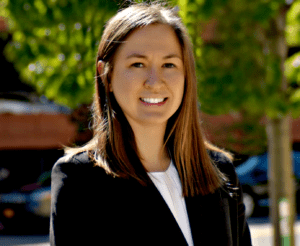 A woman in black jacket standing on sidewalk.
