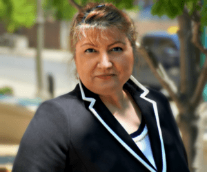 A woman in black jacket standing next to tree.