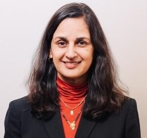 A woman in black jacket and red shirt smiling.