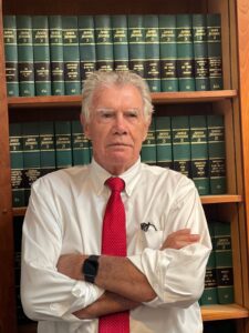 A man in front of some books wearing a red tie.