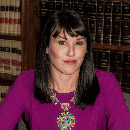 A woman in purple shirt sitting in front of book shelves.